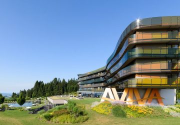 Blick auf die Balkone des AVIVA Hotels und davor der Naturschwimmteich und grüne Wiesen