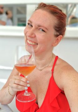 Julia in einem roten Kleid, hält ein Glas Rose Wein in der Hand und lächelt
